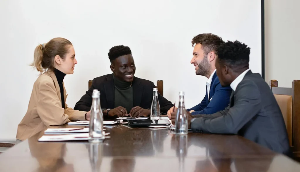 Diverse team of four smiles and converses around a boardroom table.