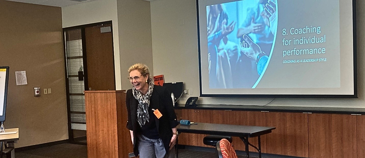 Instructor smiles while presenting a “Coaching for individual performance” slide in a classroom.